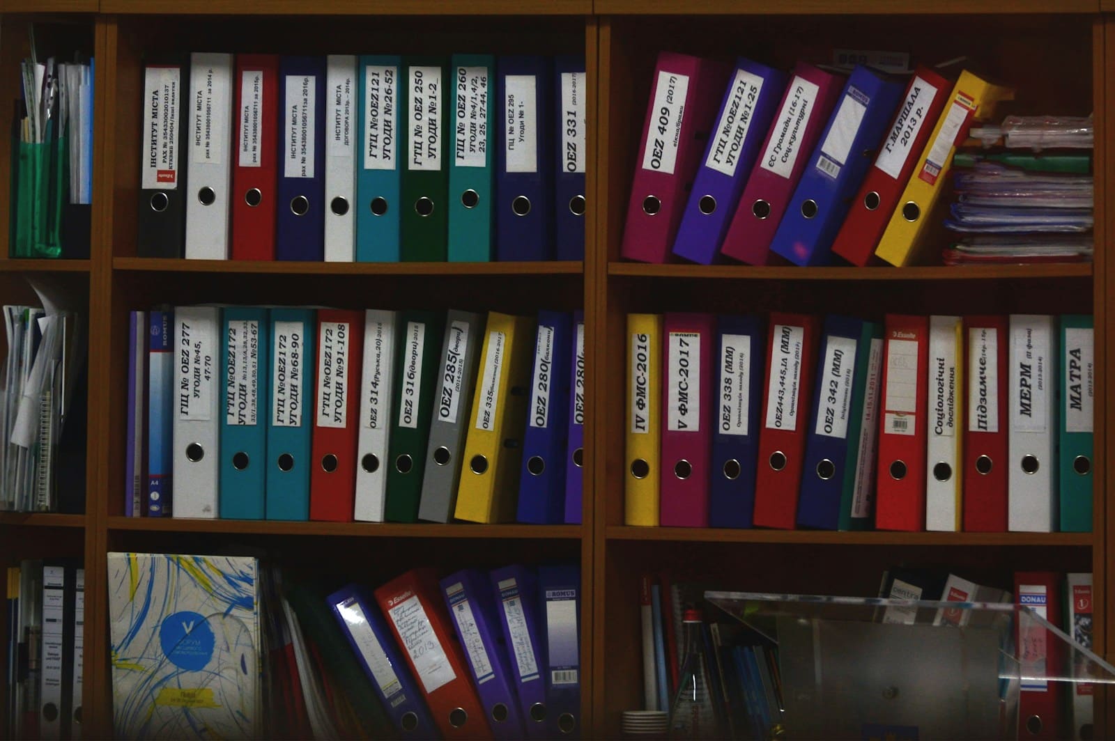 Ahşap raflarda sıralanmış renkli klasörler ve dosya arşivi